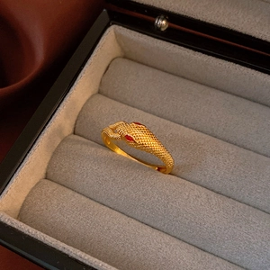Macro shot of gold snake ring with red gem eyes and scale texture on velvet