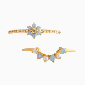 Minimalist gold ring set with blue flower petals and pearl accents on white background