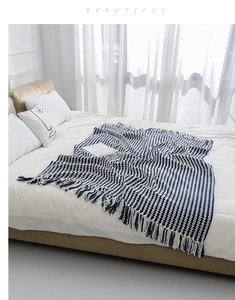 Close-up of blue and white chunky knit blanket with decorative fringe tassels on bed