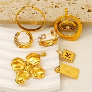 Gold titanium steel hoop earrings set with pearls and charms on stone display