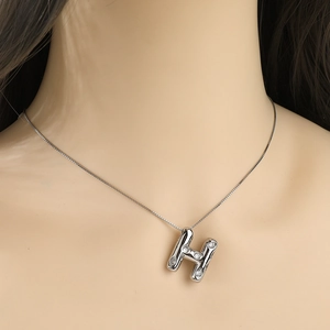 Close-up of a silver-tone necklace with an H-shaped pendant set with sparkling zircons