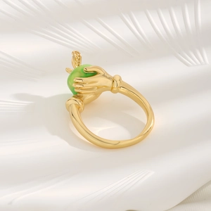 Golden hand-shaped ring holding a green apple zircon stone on a white wavy background
