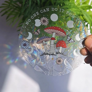 Rainbow prism suncatcher sticker with mushroom and butterfly patterns held in sunlight
