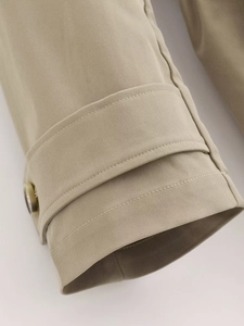 Detailed close-up of khaki trench coat cuff with amber button and twill fabric texture