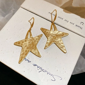 Detailed close-up of gold star earrings with a hammered metal texture on a white box