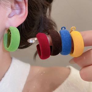 Détail de boucles d'oreilles créoles C floquées en cinq couleurs portées par un mannequin