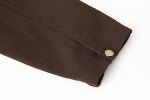 Detail der dunkelbraunen Twill-Stoffstruktur und goldener Metalldruckknopf an der Manschette