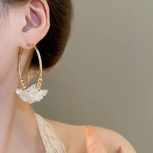 Close-up of gold hoop earrings with white acrylic flowers shown on a model's ear