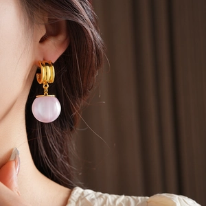 Close-up of golden irregular drop earring with pink resin ball on model's ear