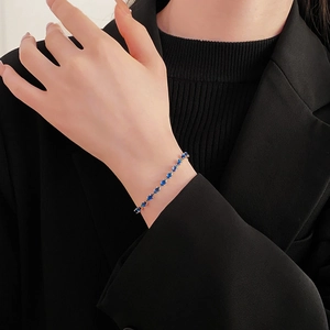 Detail of elegant gold-tone bracelet with blue gemstone on model wearing a black blazer