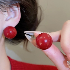 Detailed view of large glossy red round pearl stud earrings with classic silver needle design