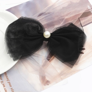 Elegant black lace bow hair clip with white pearl detail on a stylish magazine background