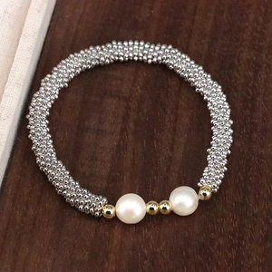 Detail view of handmade beaded bracelet with pearls and golden spacers on wooden background