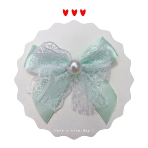 Detail of mint green satin bow hair accessory with white lace and pearl embellishment