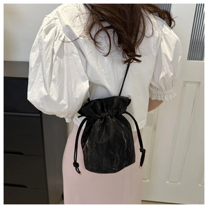 Rear view of a model wearing a black drawstring bucket bag with pleated texture detail