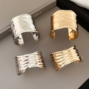 Detail of metallic textured open bangles in gold and silver finish with wave patterns