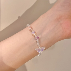 Detalle de pulsera de cuentas con dijes de corazón iridiscentes y mariposa puesta en la muñeca