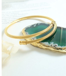 Detail of warm gold twisted rope bracelet on green mineral stone with metallic texture