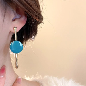 Close-up of geometric acrylic drop earrings with gold finish and teal enamel on model