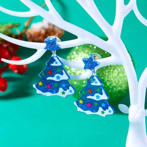 Close-up of glittery blue Christmas tree earrings with star patterns on jewelry stand