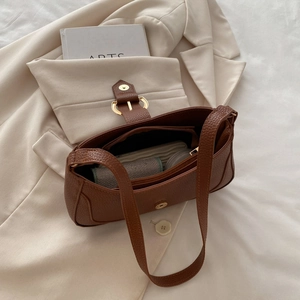 Detailed view of brown litchi pattern leather shoulder bag on a white blazer background