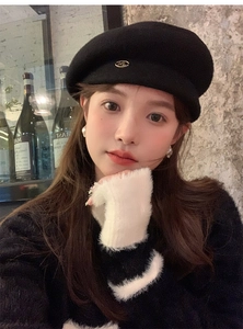 Close-up of a classic black wool beret with an 'M' metal logo on a model in autumn