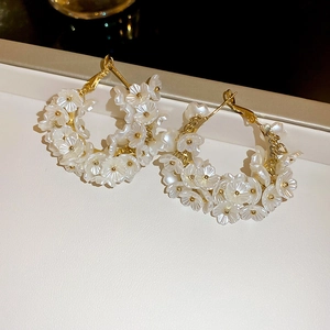 Macro detail of elegant gold hoop earrings adorned with intricate white acrylic flowers
