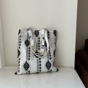 Close-up of ethnic floral embroidery and fabric texture on a white canvas tote bag