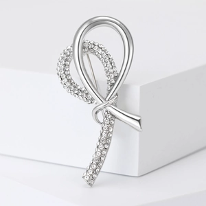 Macro detail of silver ribbon knot brooch featuring sparkling crystal inlay on white stand