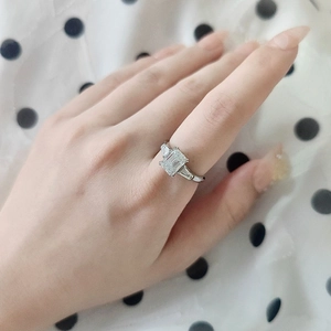Close-up of a 2-carat emerald cut moissanite silver ring on a finger with side stones