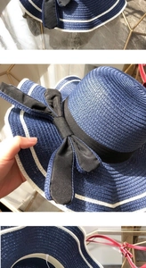 Detail of navy straw hat with fine spiral weave, black bow ribbon and white striped edge