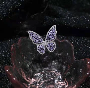 Macro detail of silver butterfly ring with purple stones and zircon on pink glass tray