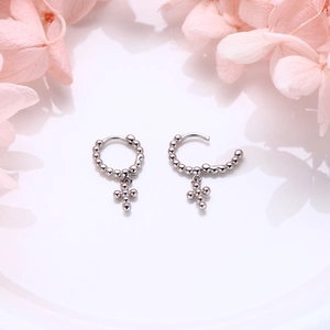 Close-up of S925 sterling silver hoop earrings with beaded cross pendant and polished finish