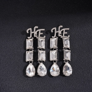 Macro detail of silver dangle earrings with HE letters and teardrop crystal pendants