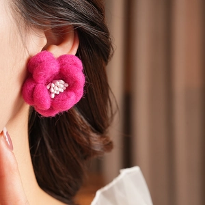 Détail de la boucle d'oreille fleur en feutre de laine rose avec pistils blancs sur modèle