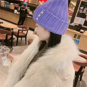 Detailed view of purple chunky knit beanie with white X-shaped embroidery accents