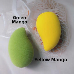 Close-up of green and yellow mango-shaped makeup sponges on a white fabric background