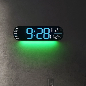 Modern LED digital wall clock with blue display and green ambient light on concrete wall