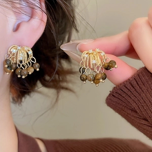 Detail of golden tassel earrings with tiger eye beads shown on model and held in hand