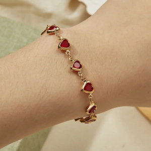 Detailed view of red heart charms on a golden link chain bracelet worn on a female wrist