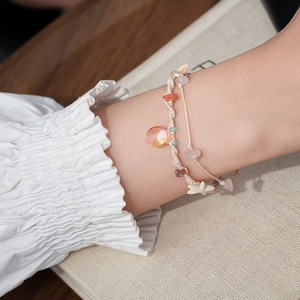 Detail of woven bracelet with orange teardrop beads, starfish charm, and natural stones