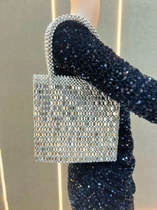 Close-up of silver metal sequin handbag held by a model in a black sequin party dress