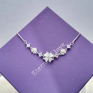 Macro shot of silver four-leaf clover necklace with white petals on a purple jewelry box