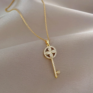 Detail of a gold key necklace with a clover design and sparkling crystals on soft fabric