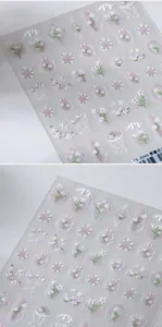 Macro shot of 3D embossed nail art stickers featuring white flowers and purple grid patterns