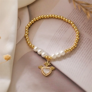 Detail of gold beaded bracelet featuring a shell heart wing charm and white pearls