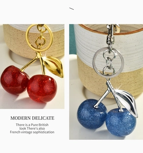 Detail of cherry keychains with red and blue glitter finish and metallic leaf accents