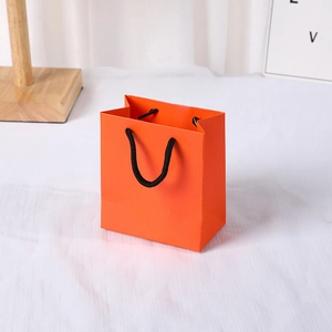 Minimalist orange jewelry gift bag with black rope handles on white textured surface