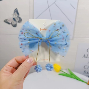 Détail d'une pince à cheveux nœud en résille bleu clair avec paillettes et pendentifs pompons