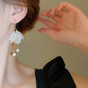 Détail de boucles d'oreilles pétales givrés blancs avec perles et glands dorés élégants